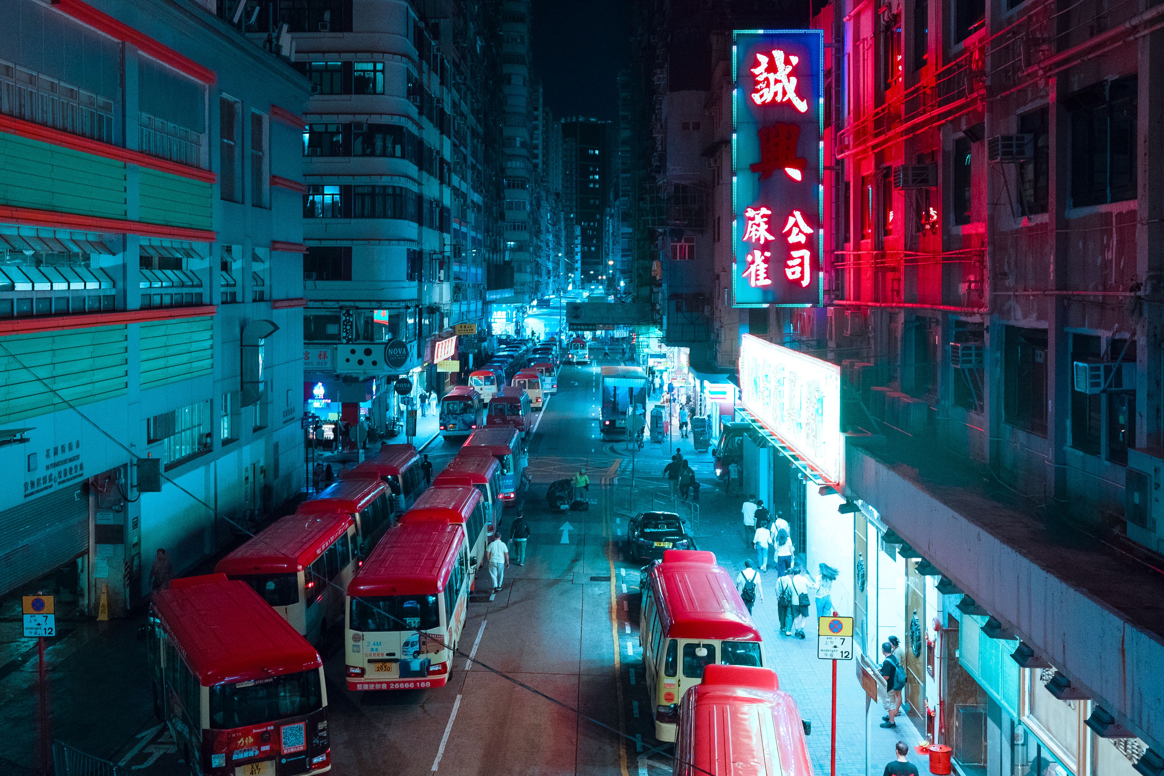 Colorful nighttime city street with buses and neon signs in an Asian cityscape.