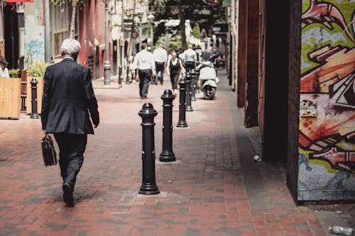 Man in Black Suit Walking on Sidewalk