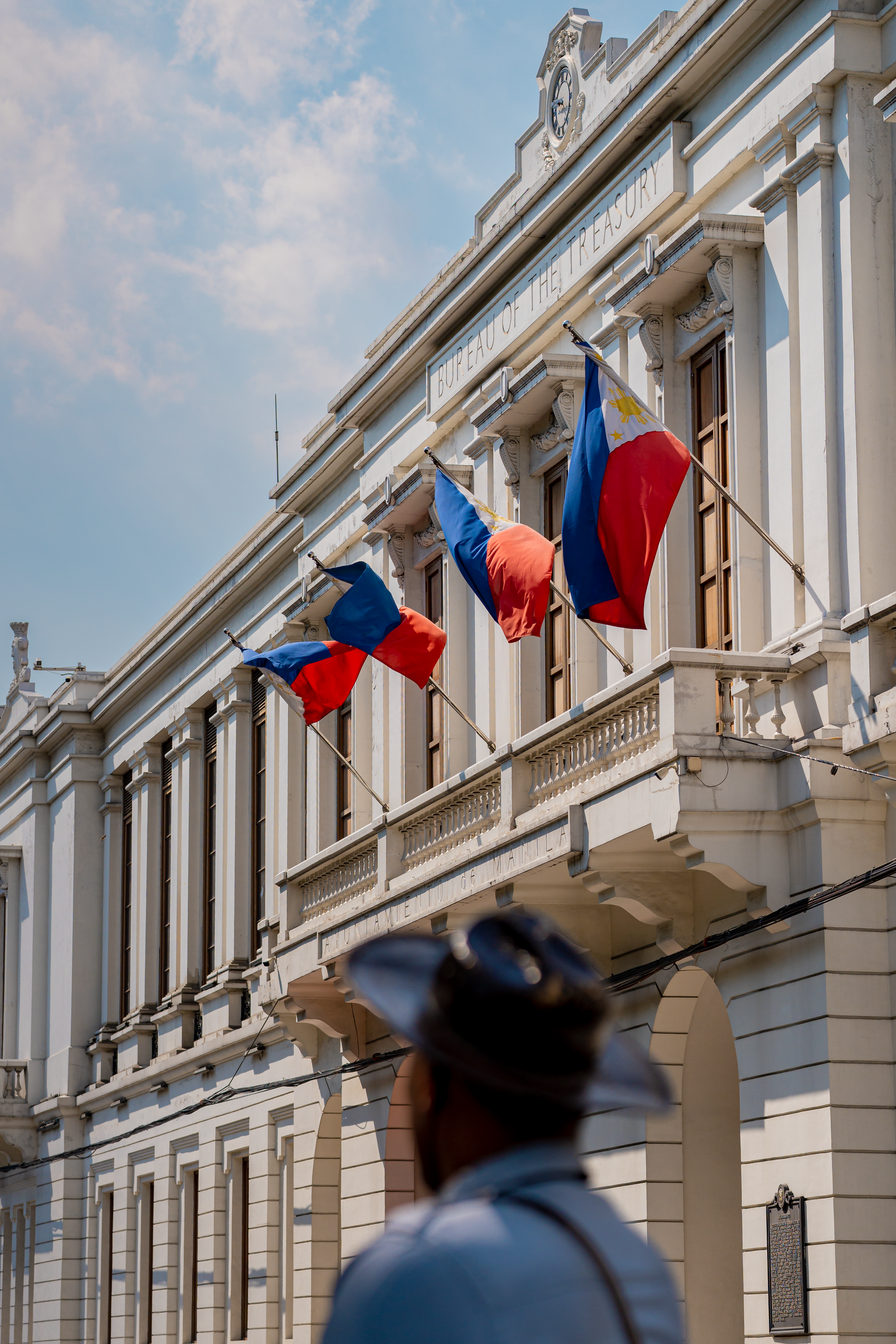 Historic building in Manila with Philippine flags on display, clear blue sky background.
