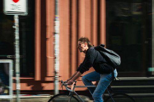 Free A young man rides a bicycle down a city street, demonstrating urban lifestyle. Stock Photo