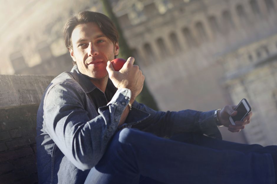 A young man enjoys a fresh apple and smartphone outdoors on a sunny day, embracing relaxation. A young man enjoys a fresh apple and smartphone outdoors on a sunny day, embracing relaxation.
