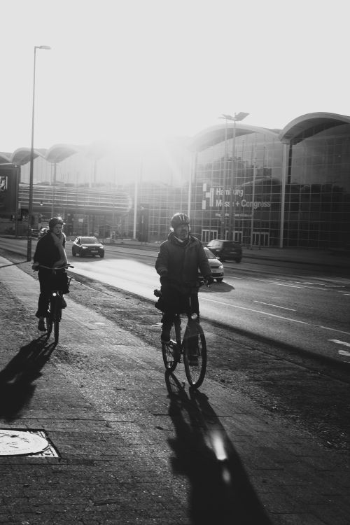 Free Black and white photo of cyclists riding outside Hamburg Messe in sunlight. Stock Photo