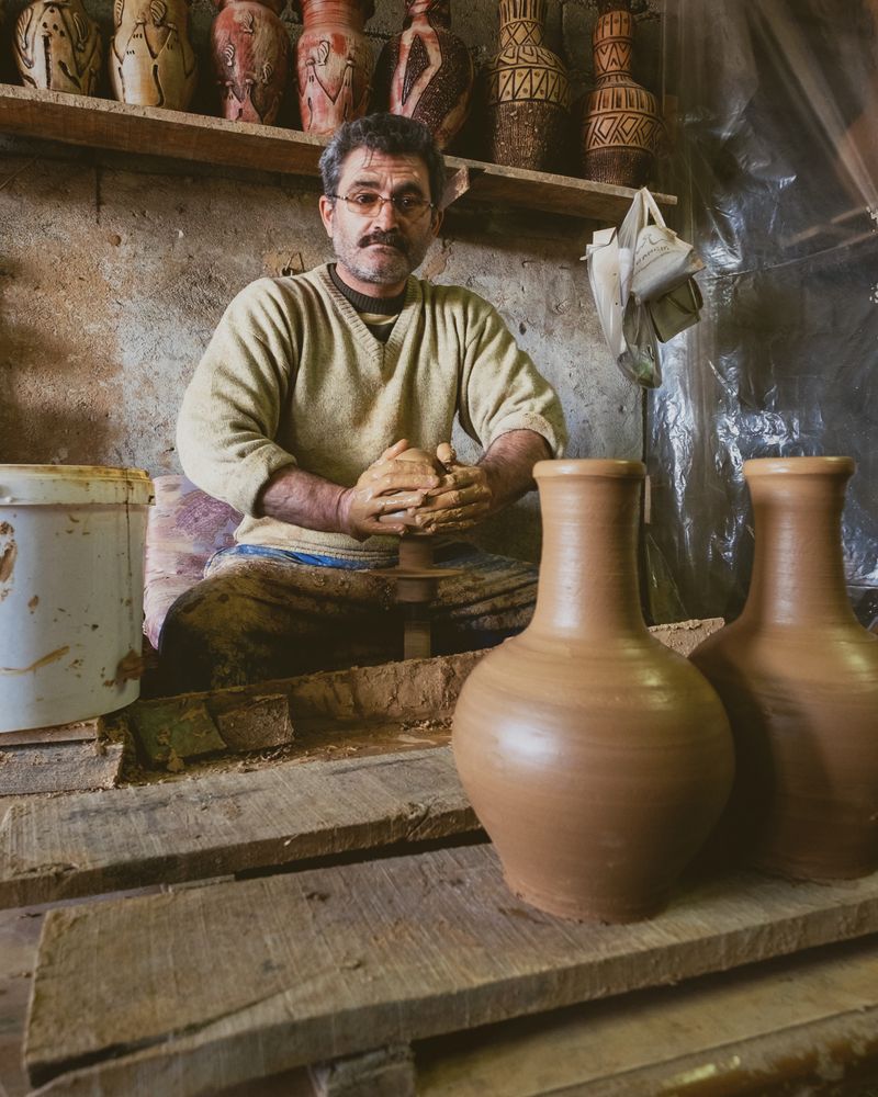 A potter seated beside two brown clay vases in his workshop
