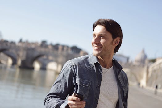 一个开朗的男人在阳光明媚的日子里，站在河边户外，背景是一座历史悠久的桥梁