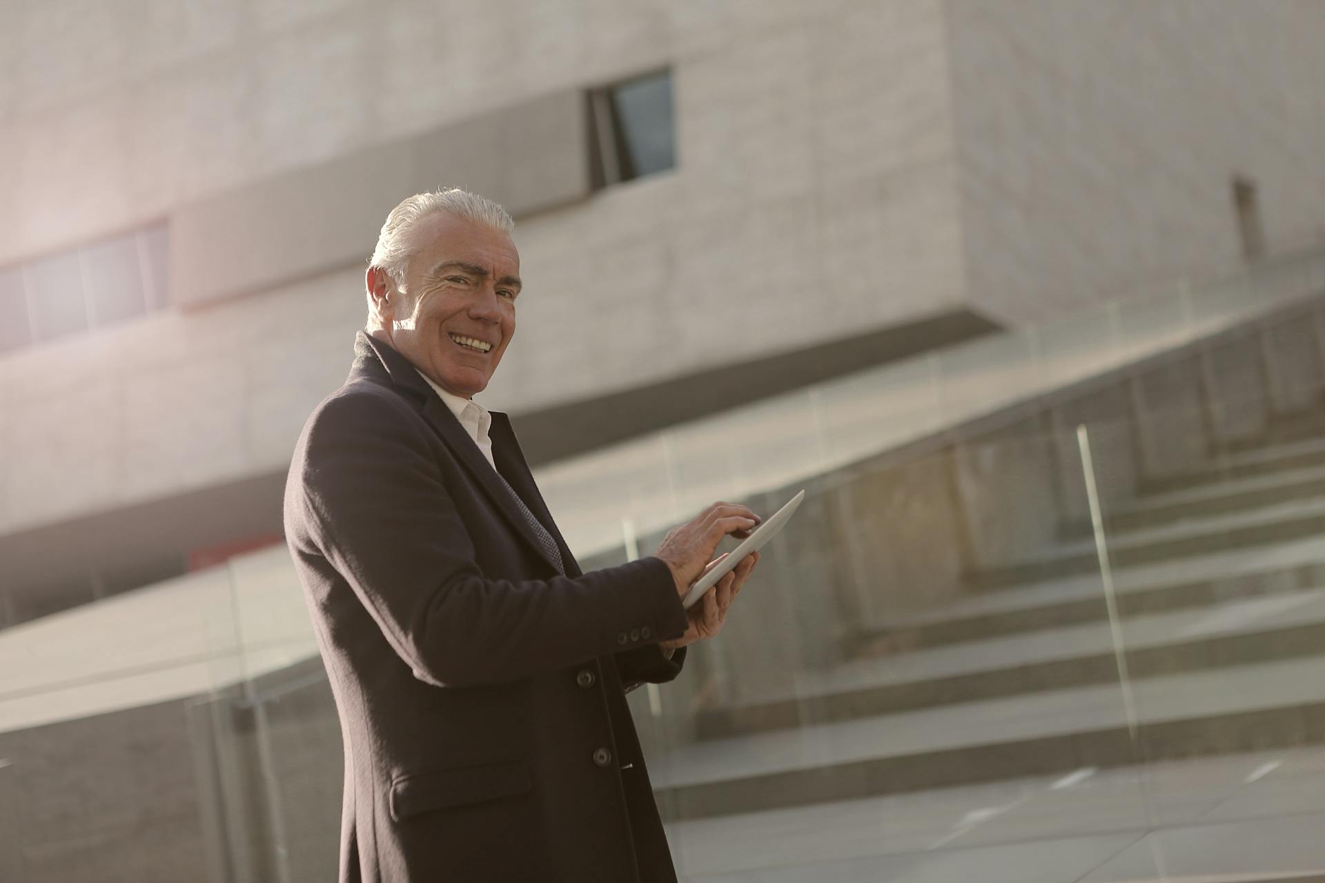 Smiling senior businessman using a tablet in an urban outdoor setting.