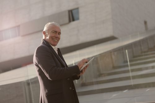 Free Smiling senior businessman using a tablet in an urban outdoor setting. Stock Photo