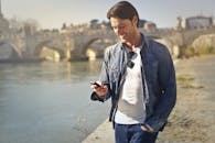 一名休闲男子在历史悠久的河边大桥附近微笑着使用智能手机