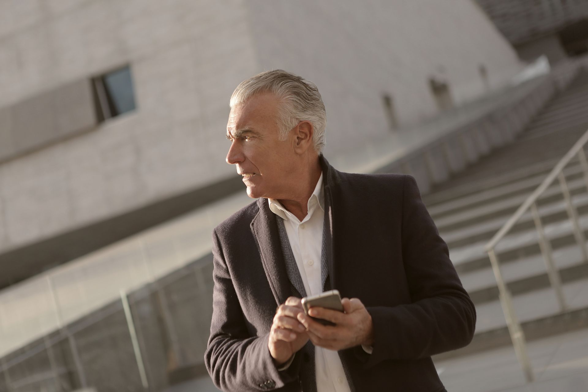 Confident senior businessman using a smartphone outdoors in modern setting.