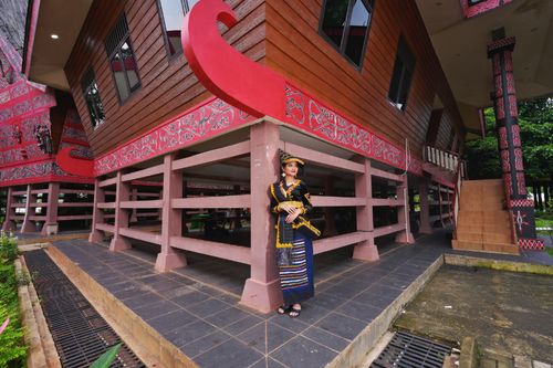 Free Woman in traditional Batak attire standing by distinctive Batak house in Jakarta, Indonesia. Stock Photo