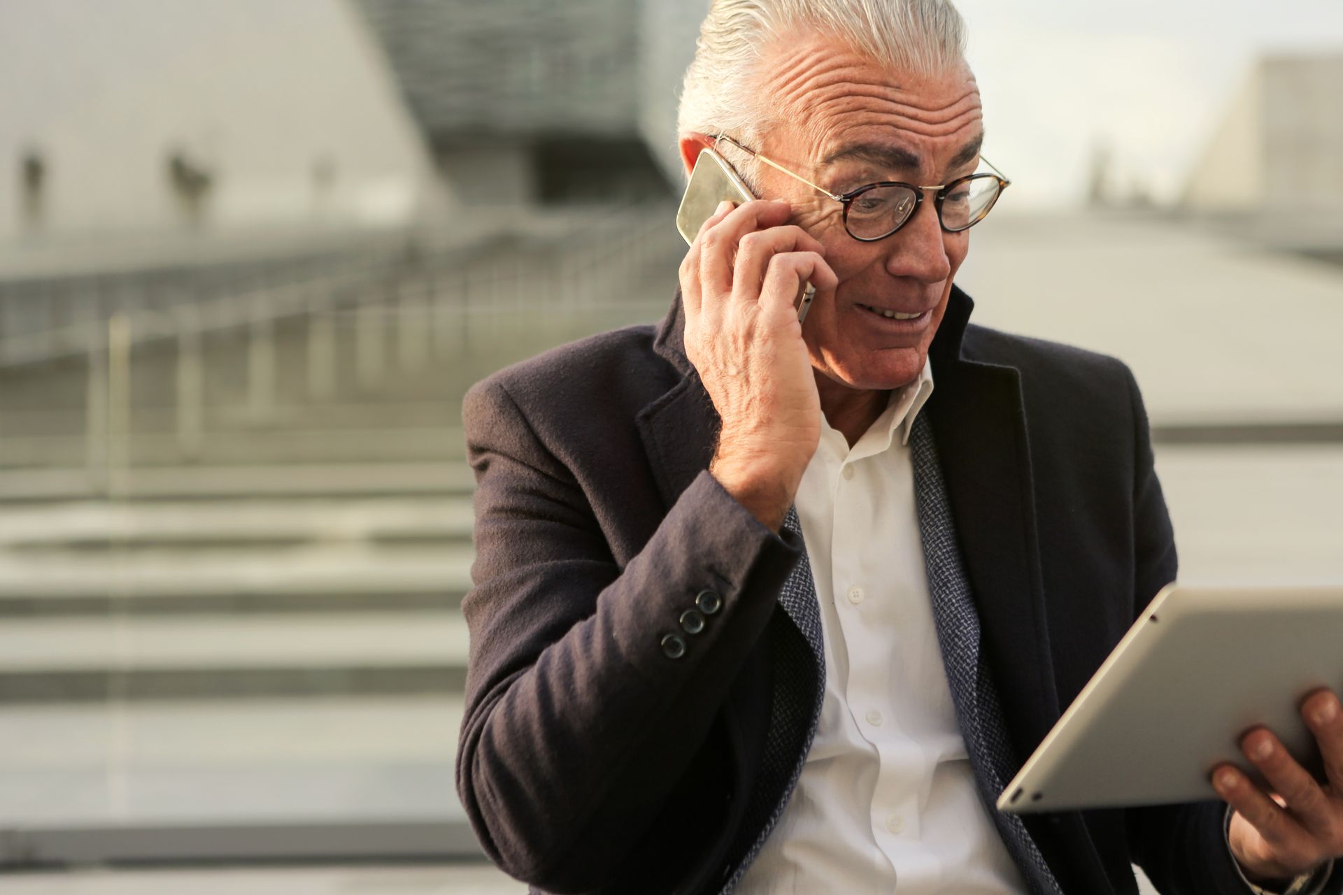 A senior man using a smartphone and tablet outdoors, showcasing modern technology engagement.