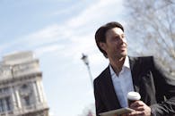 在城市环境中，商人手持平板电脑，品味咖啡，散发着自信与现代感