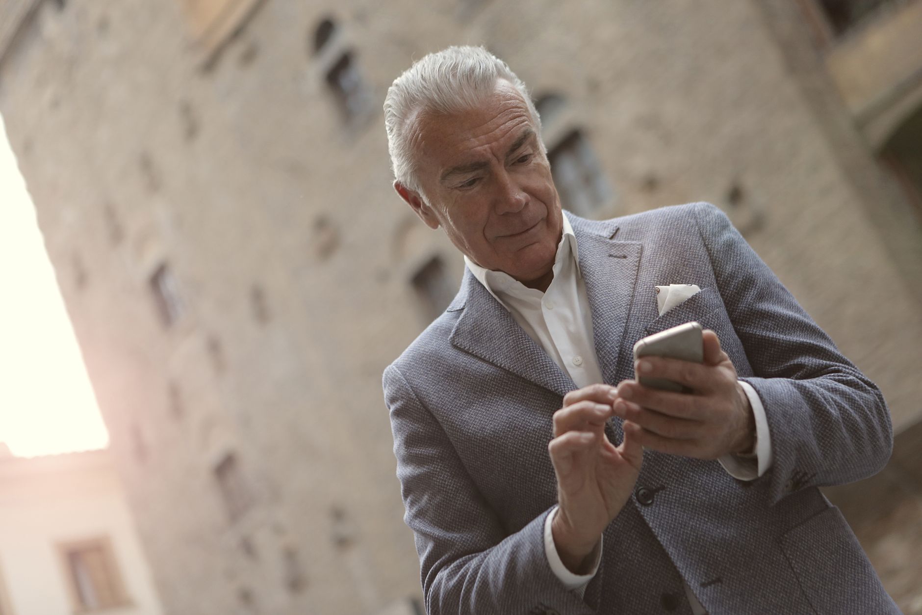 전남 어르신 스마트폰 무료 교육, 섬·농촌 지역까지 무료 교육 찾는 법 3 Senior man in a suit using a smartphone outside a historic building during the day.