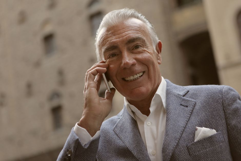 Elderly businessman smiling while talking on smartphone outdoors. Professional attire and modern technology in use.