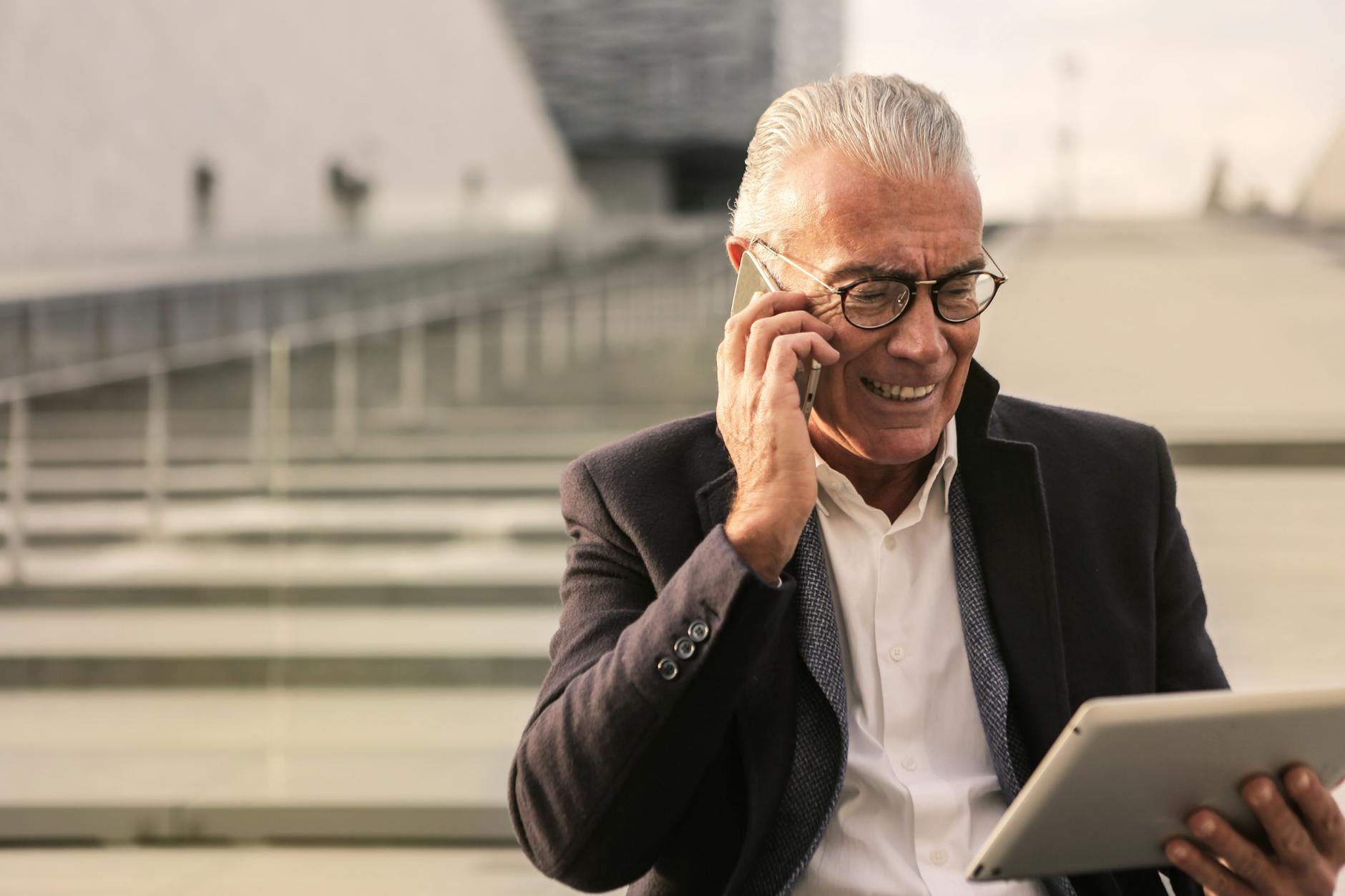 울산 어르신 스마트폰 무료 교육 4 Elderly man in business attire using smartphone and tablet, smiling outdoors.