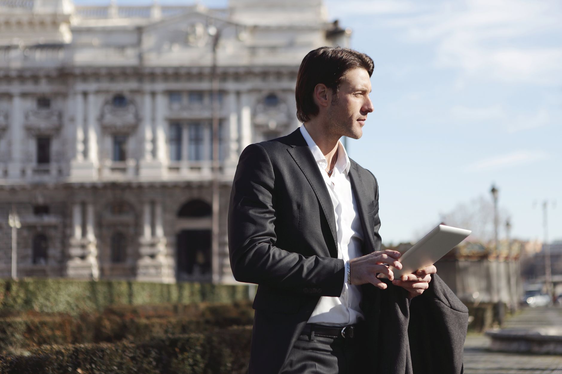 Elegant man with tablet outside historical building, exuding professional charm.