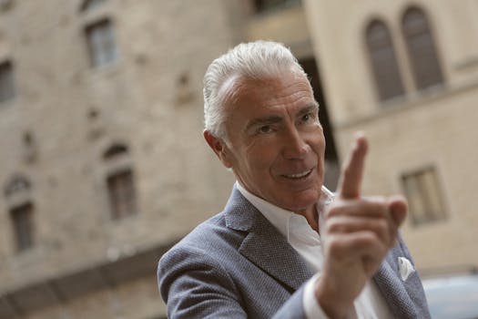 一位白发、西装革履的高级男子在背景模糊的城市户外环境中摆出手势