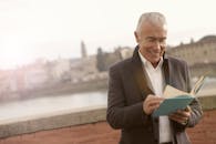 在背景模糊的城市环境中，一位微笑的老年人正在看书