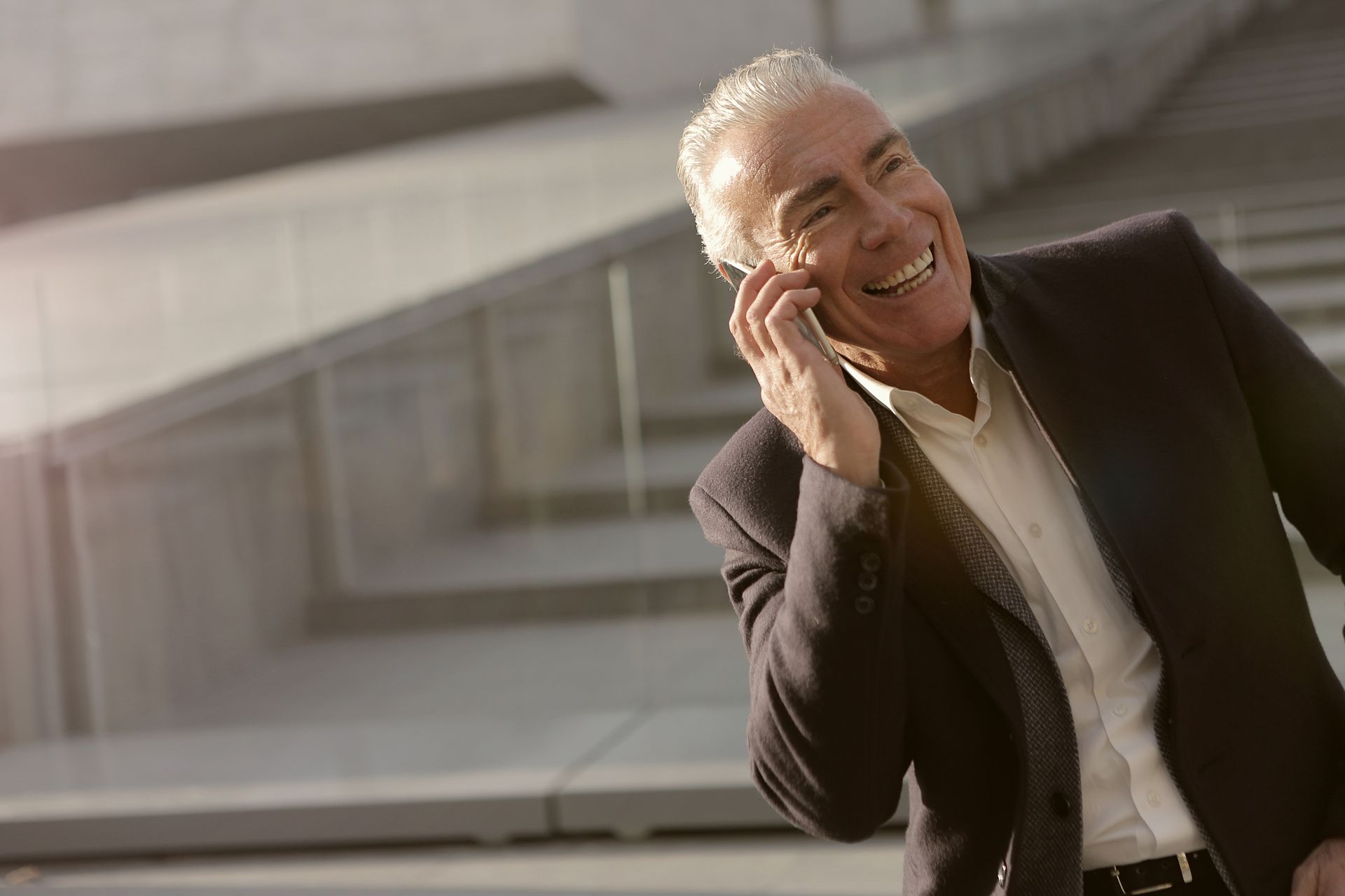 Senior businessman enjoying a mobile phone conversation outdoors with a smile.