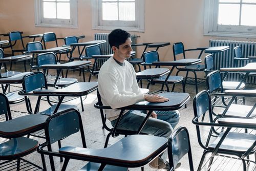Free A thoughtful student sits alone in a Buenos Aires classroom filled with empty desks, capturing a moment of reflection. Stock Photo