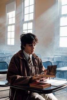 A young adult student reads in a sunlit Buenos Aires classroom, surrounded by books on a desk.