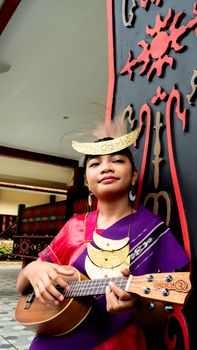 A woman in traditional Indonesian attire plays a ukulele in Jakarta. - Fotografer Sidoarjo