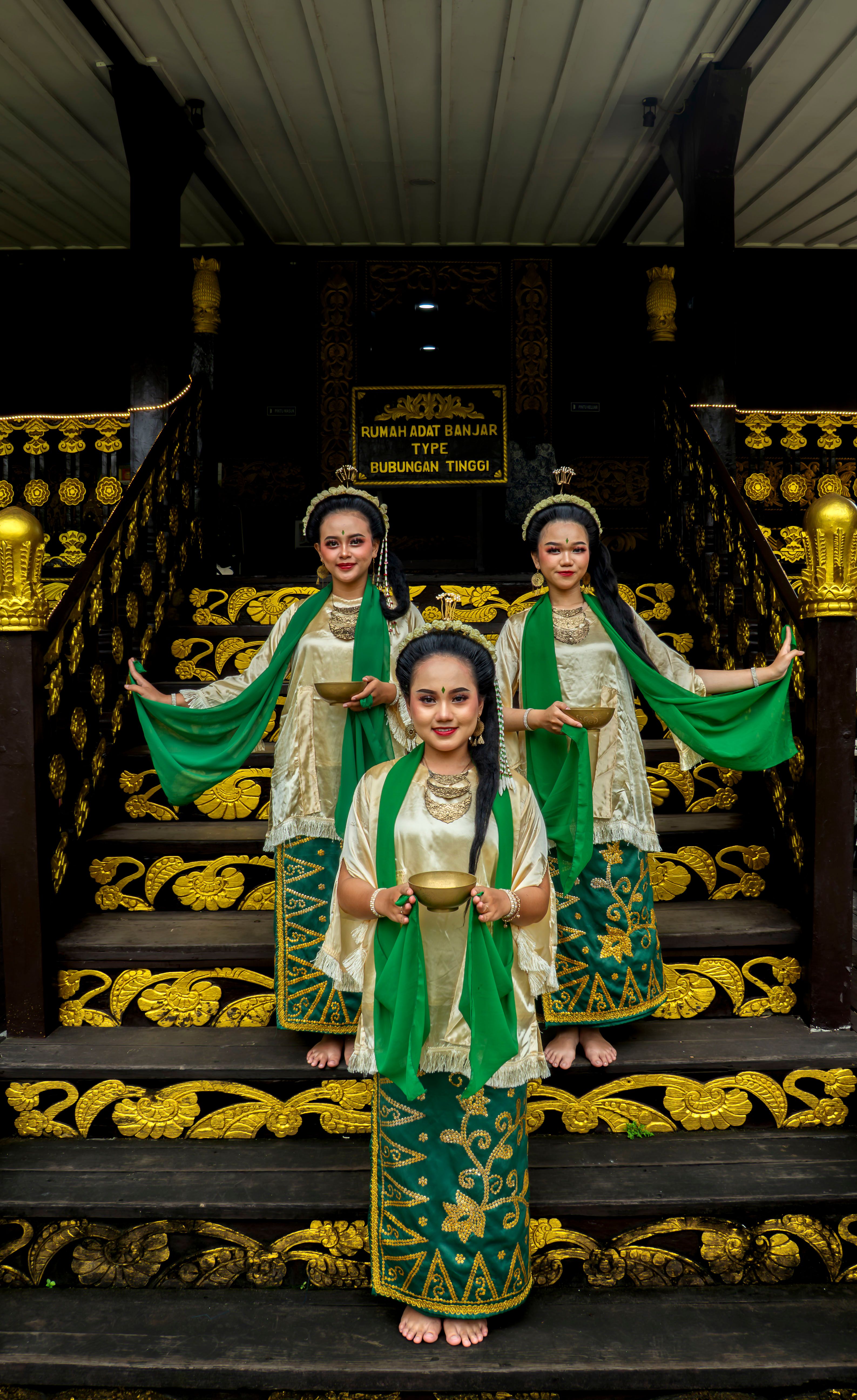 Three women in traditional Indonesian attire performing a cultural dance at Rumah Adat Banjar.