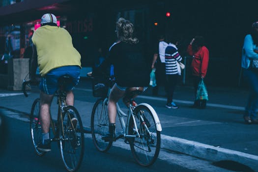 Two cyclists biking on a busy urban street with pedestrians nearby.