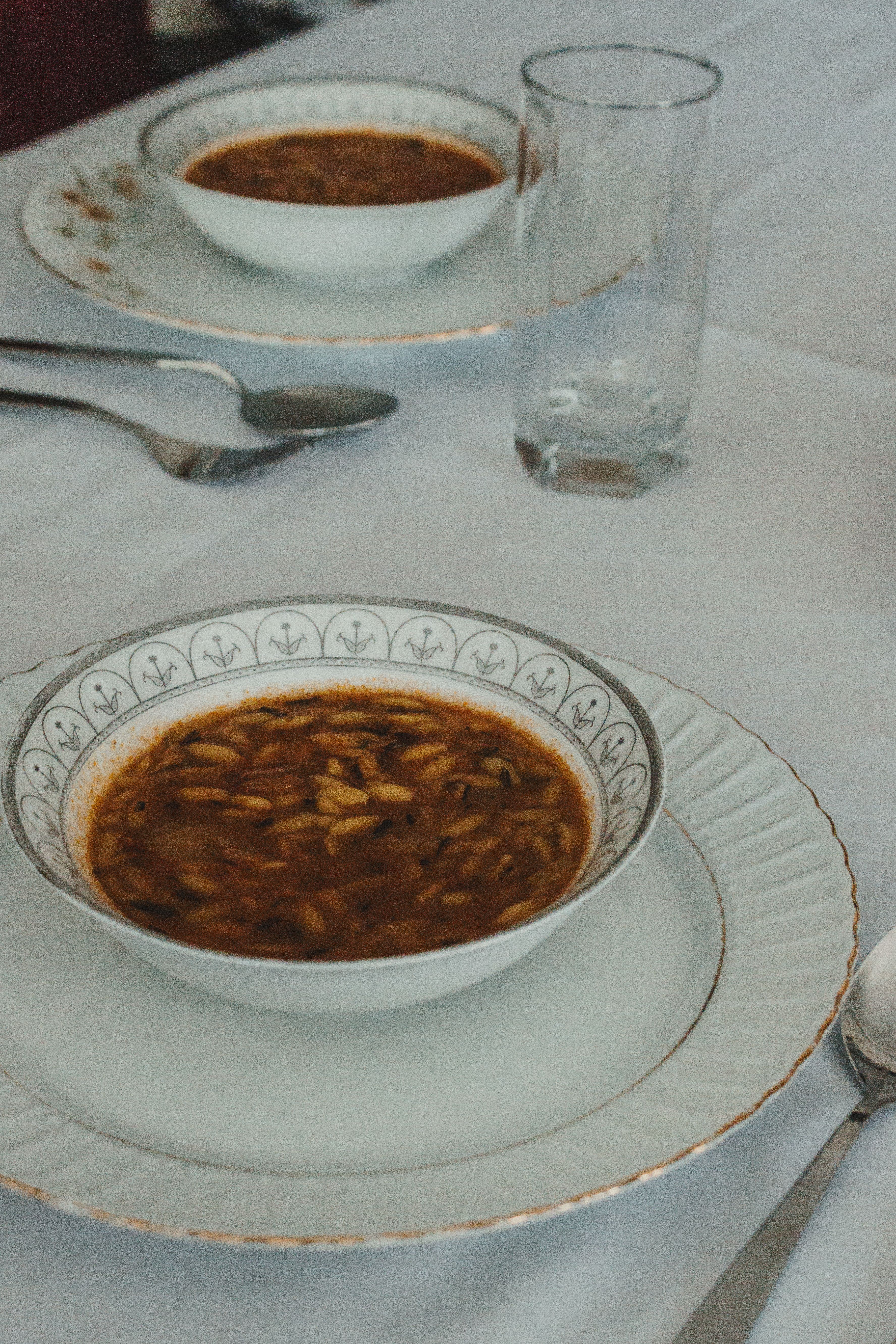 A stylish table setting featuring soup in decorative china bowls on a white tablecloth.