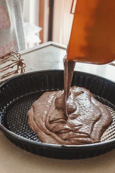 Close-up of chocolate cake batter poured into a baking pan with a whisk nearby.