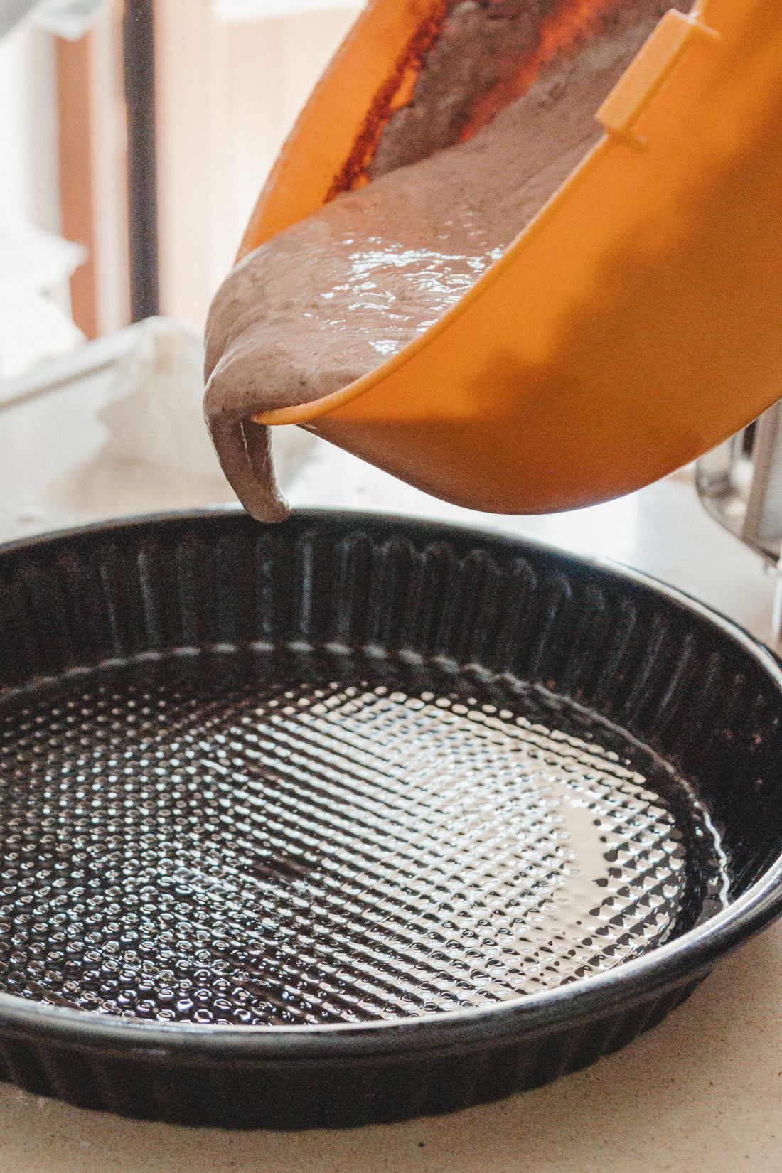 Cake batter pouring from orange bowl into black fluted tart pan