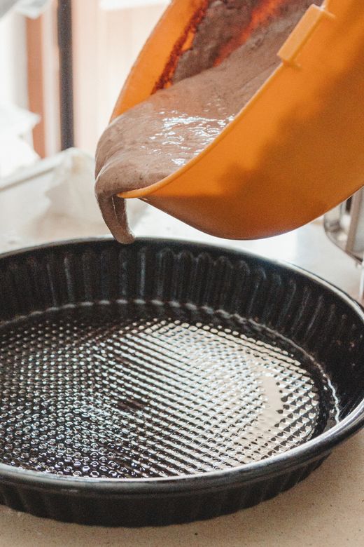 Cake batter pouring from orange bowl into black fluted tart pan