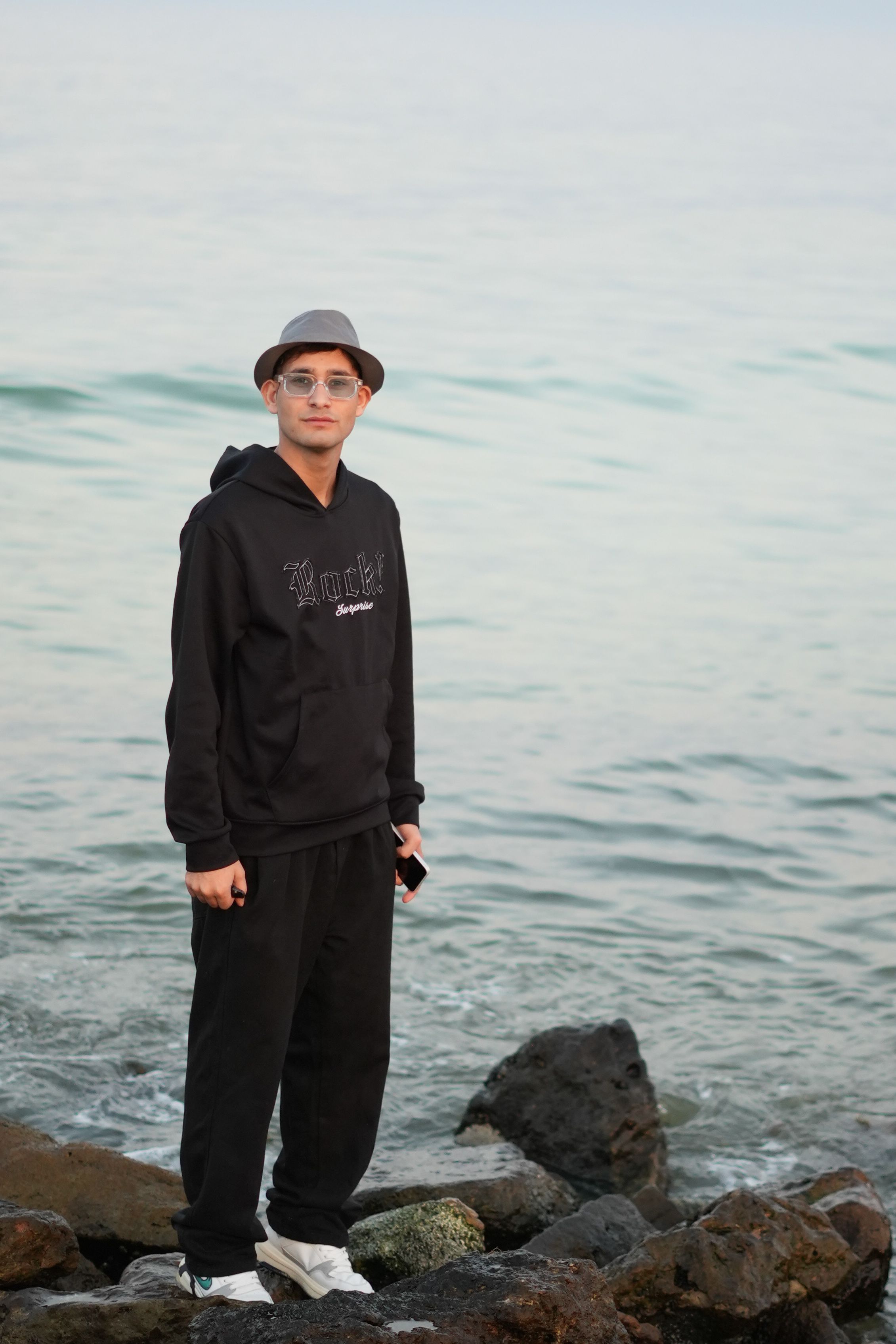 Man in casual attire stands on rocky shoreline by the sea in Saudi Arabia. Calm and serene atmosphere.