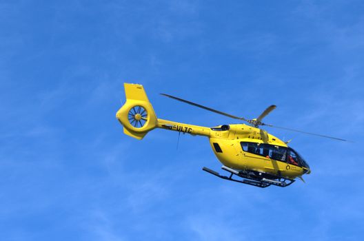 Bright yellow helicopter in flight against a clear blue sky.