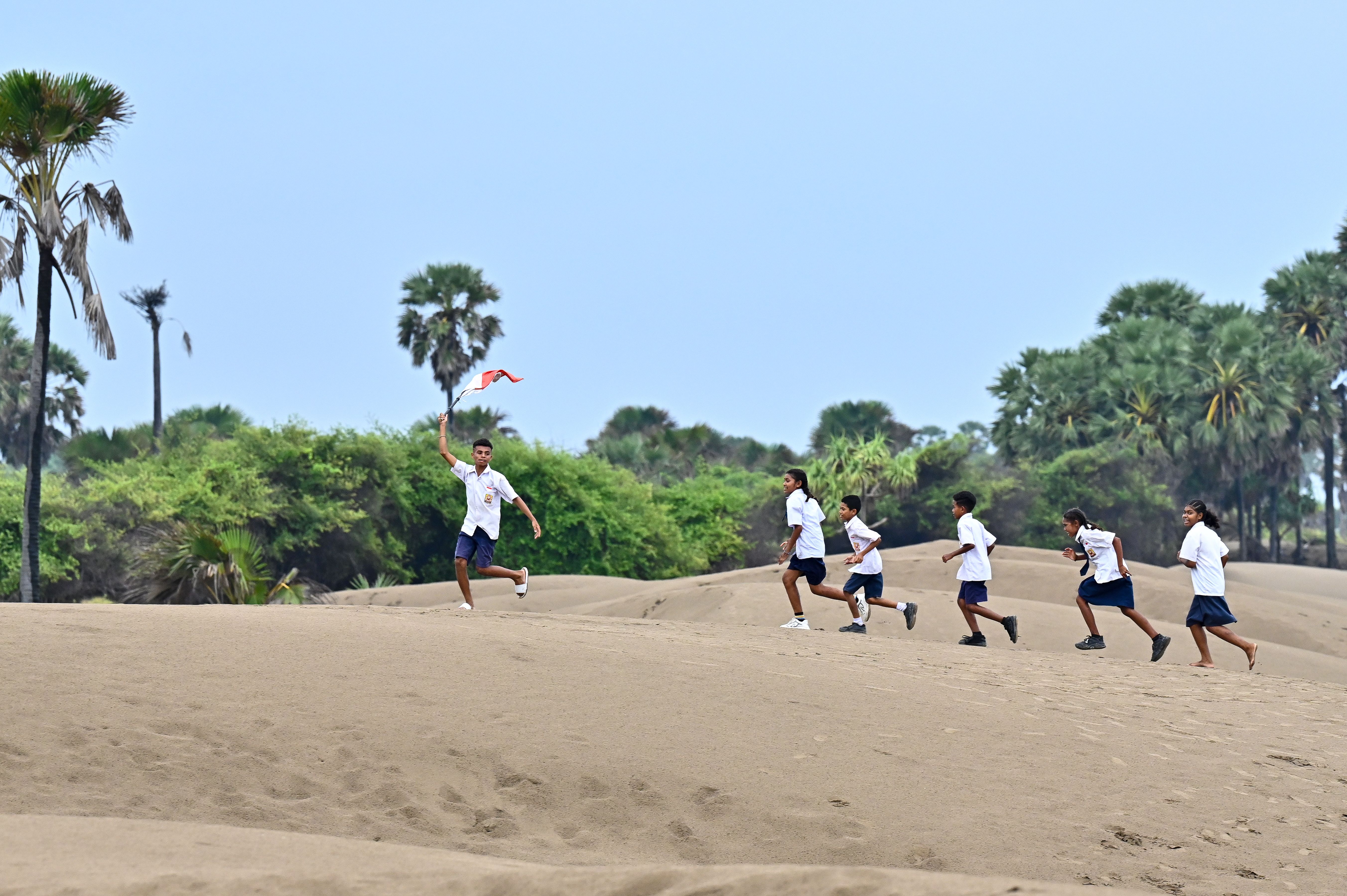 A group of children joyfully runs across sand dunes, carrying the Indonesian flag in East Nusa Tenggara.