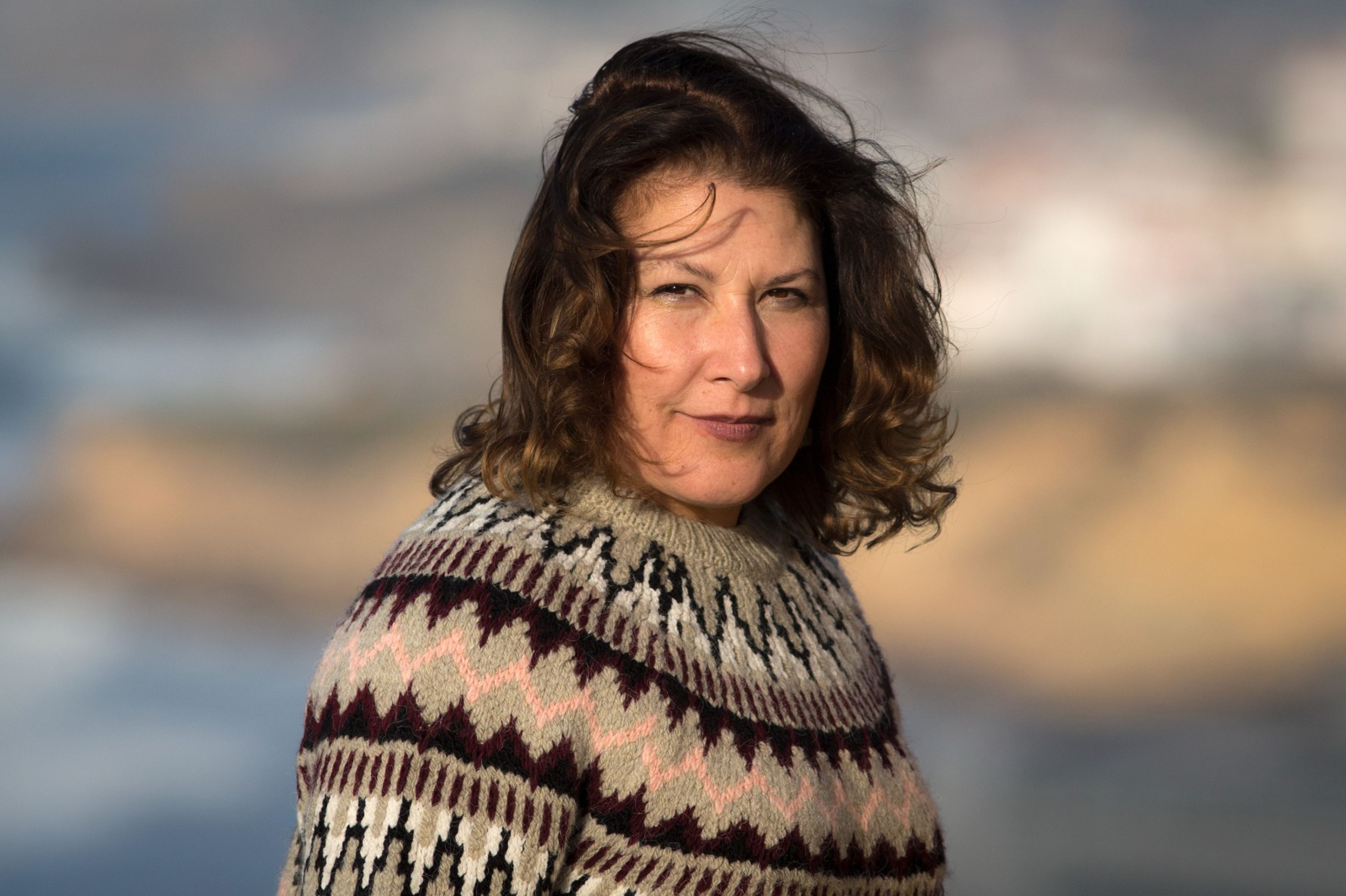 Close-up portrait of a woman outdoors wearing a patterned sweater in soft, natural light.