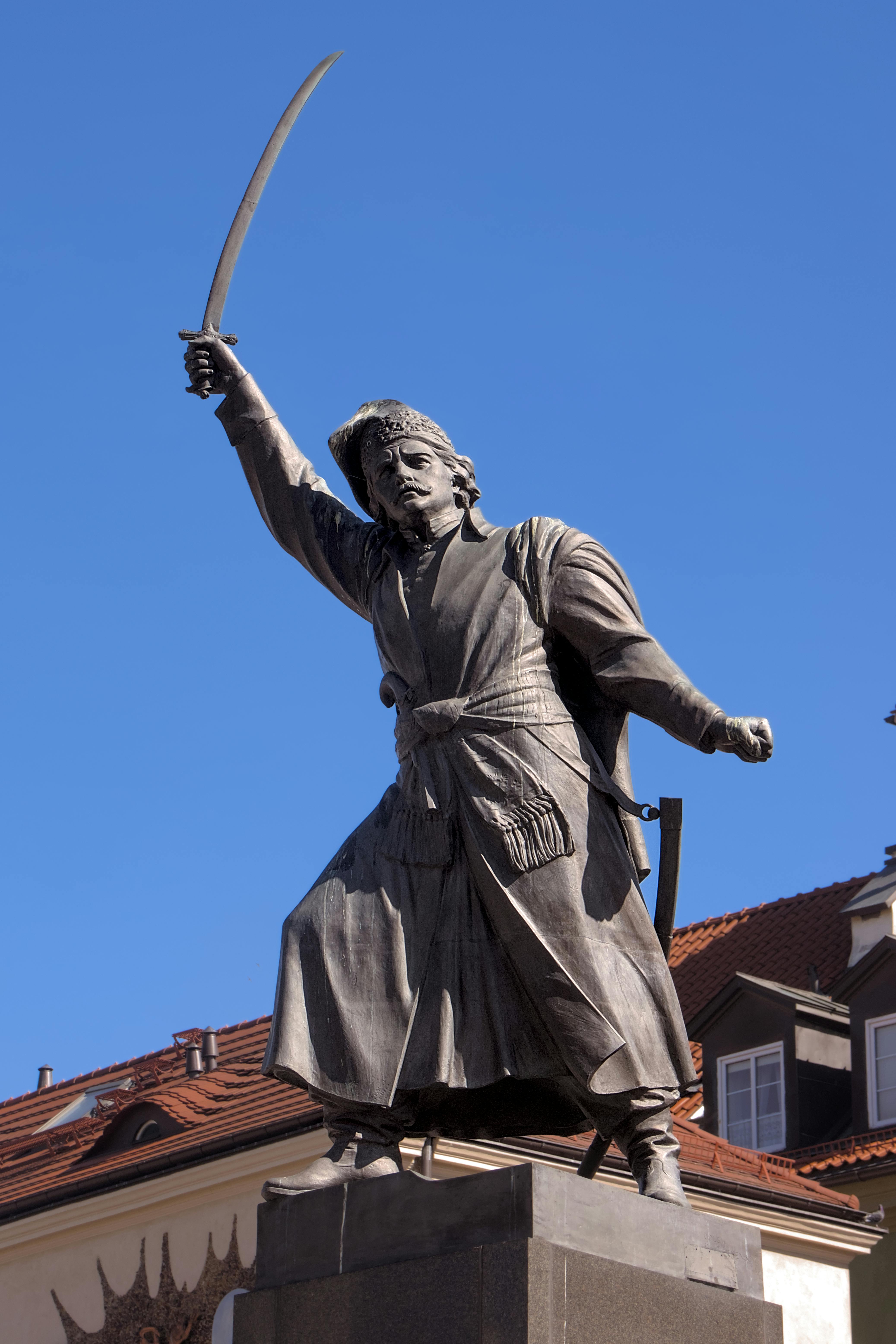 The iconic statue of Jan Kiliński against a blue sky in historic Warsaw.