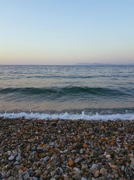Peaceful pebble beach scene with gentle waves at sunset, capturing natural serenity.