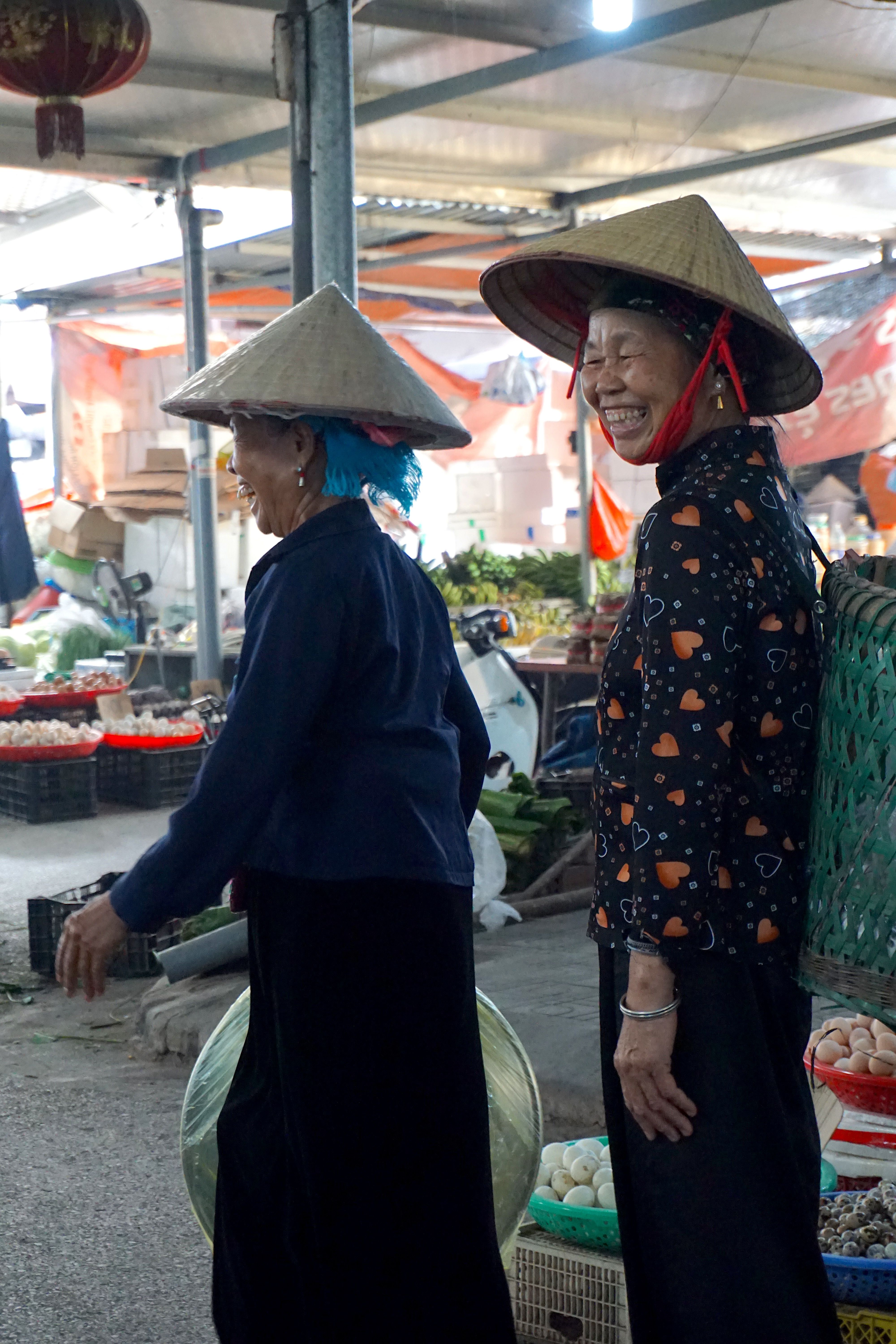 Two women wearing conical hats at a bustling market in Nghia Lo, Vietnam.