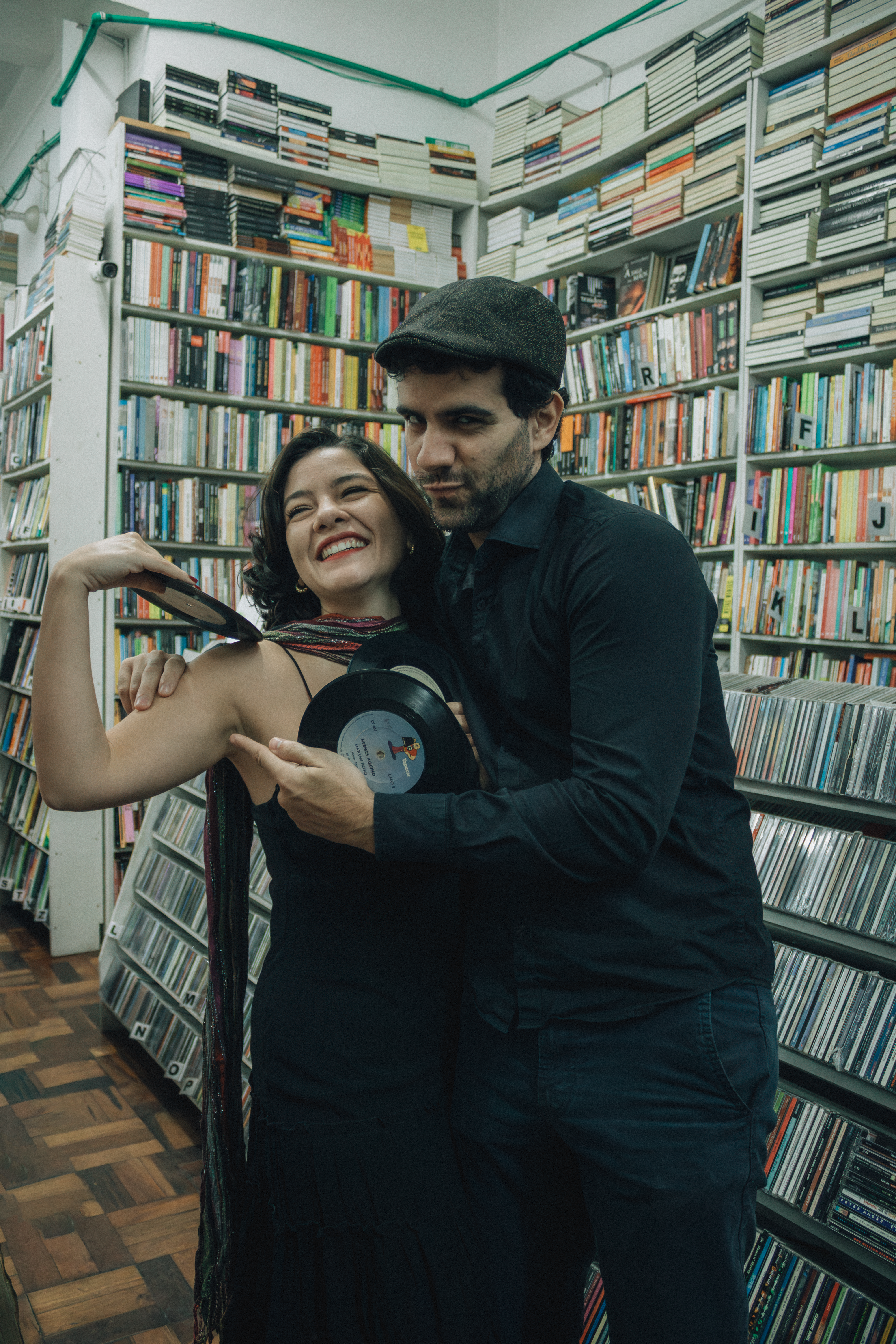 Smiling couple with vinyl records in a cozy bookstore surrounded by books and CDs.