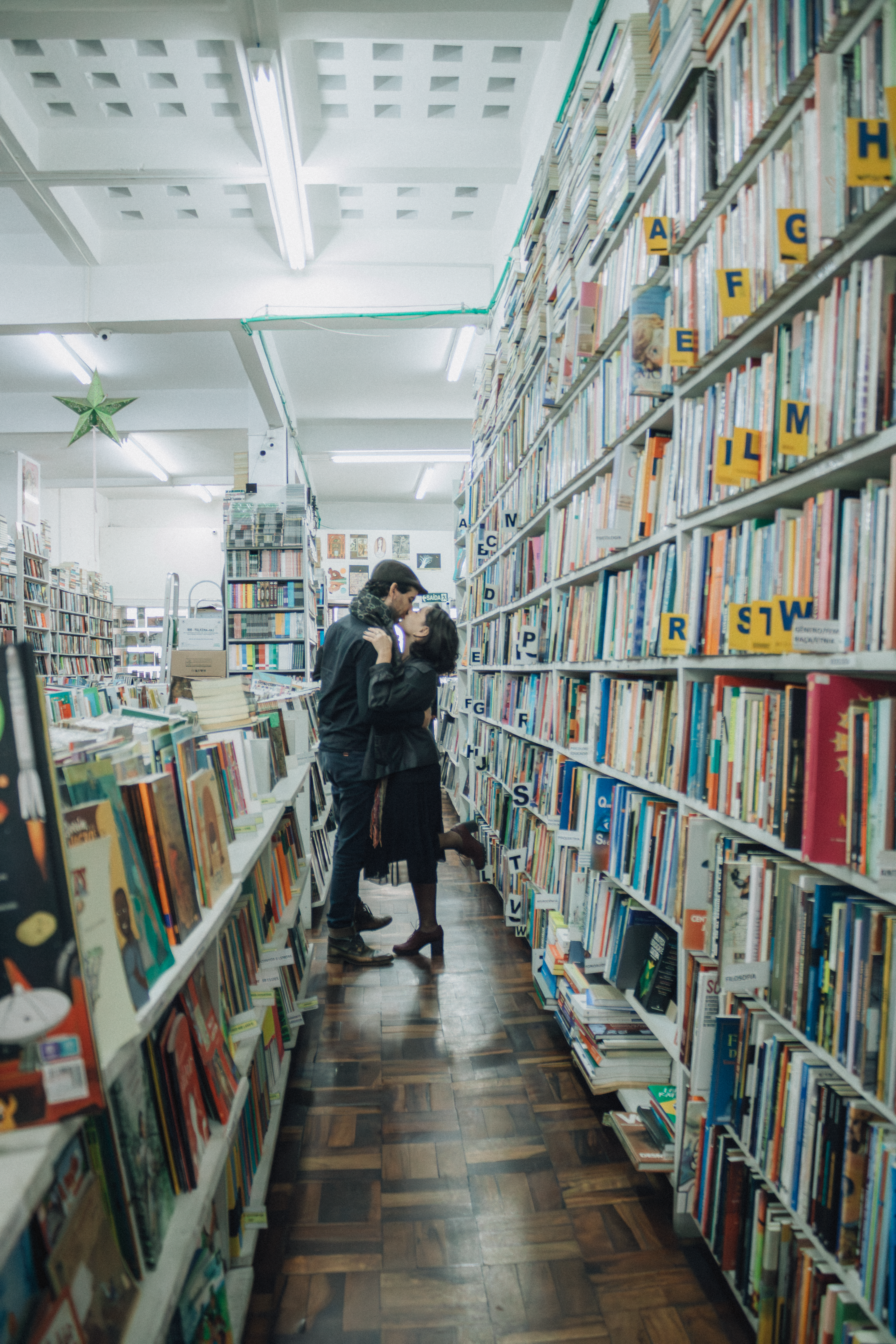 Romantic couple kissing in a cozy library aisle filled with books, creating an intimate atmosphere.