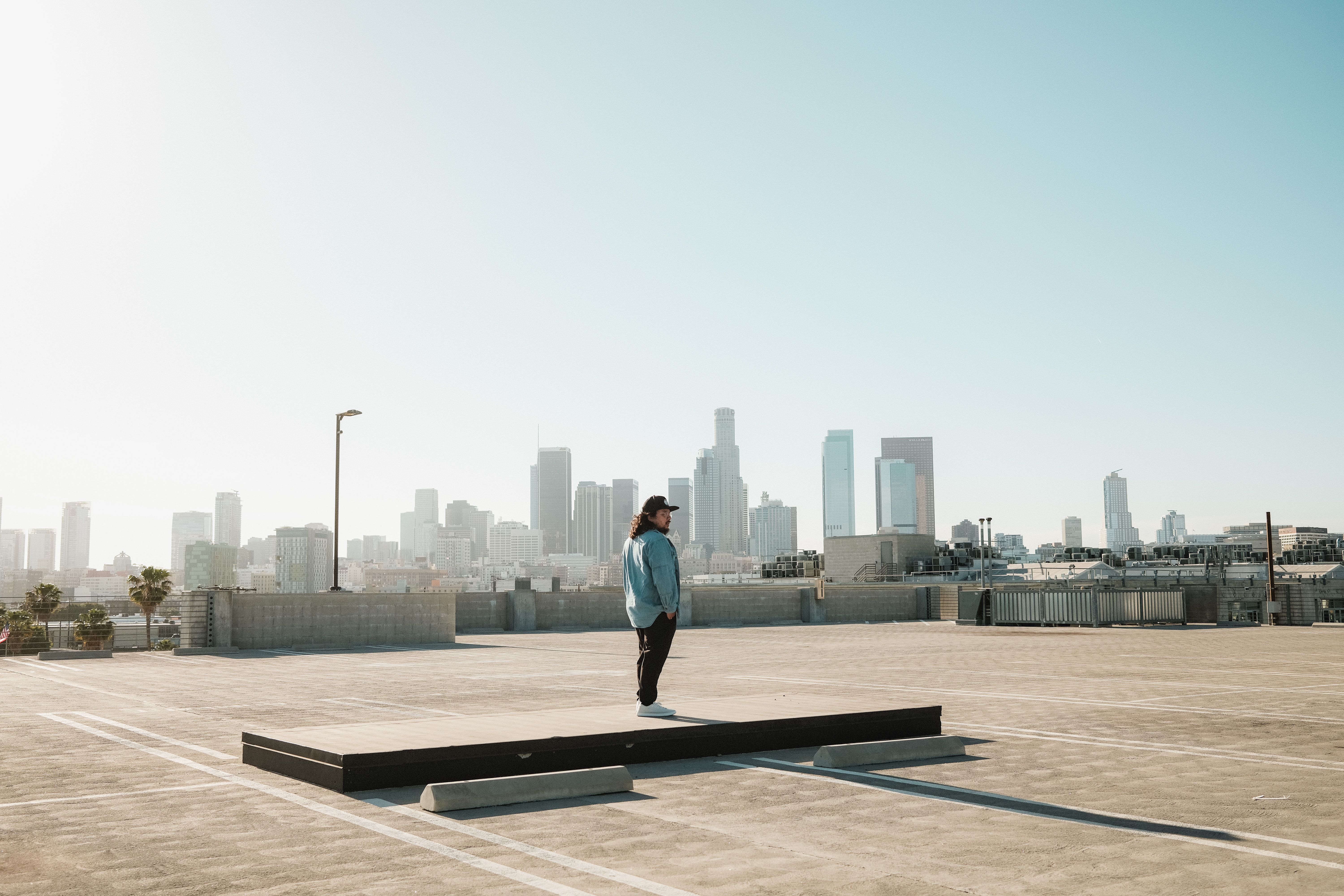 A solitary figure stands on a rooftop with a panoramic view of Los Angeles' skyline.