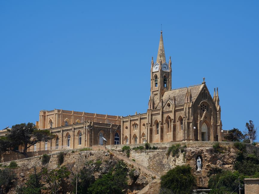 A picturesque Gothic-style church on a hilltop in Malta under a clear blue sky.