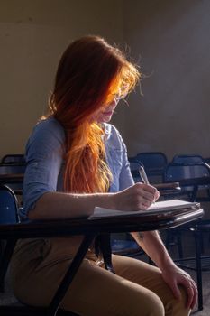 A young woman with red hair studies in a sunlit classroom in Buenos Aires, Argentina.