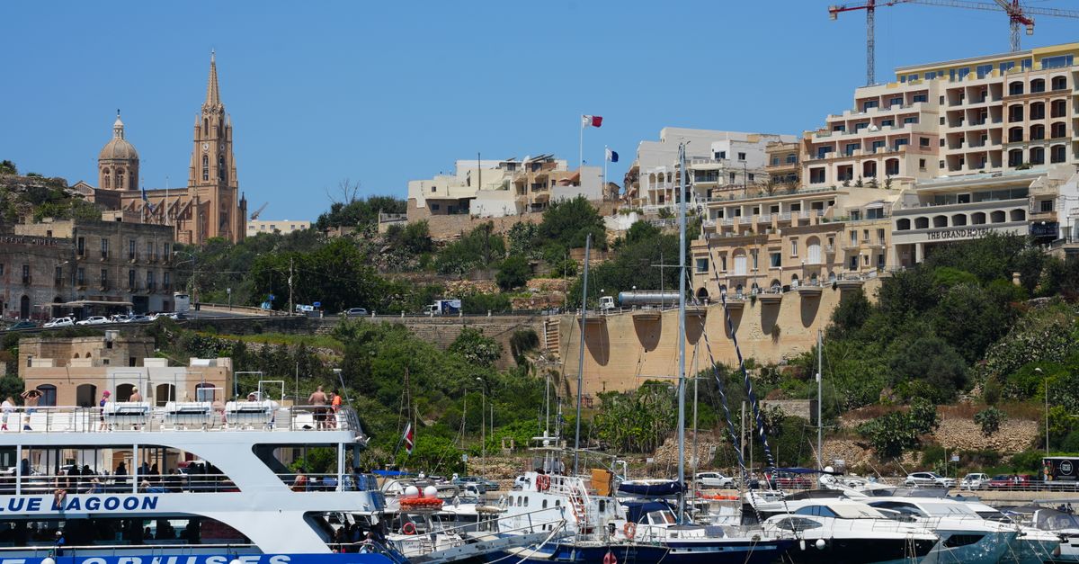 Boats docked at Mgarr Harbour in Gozo, Malta with church and buildings in the background.