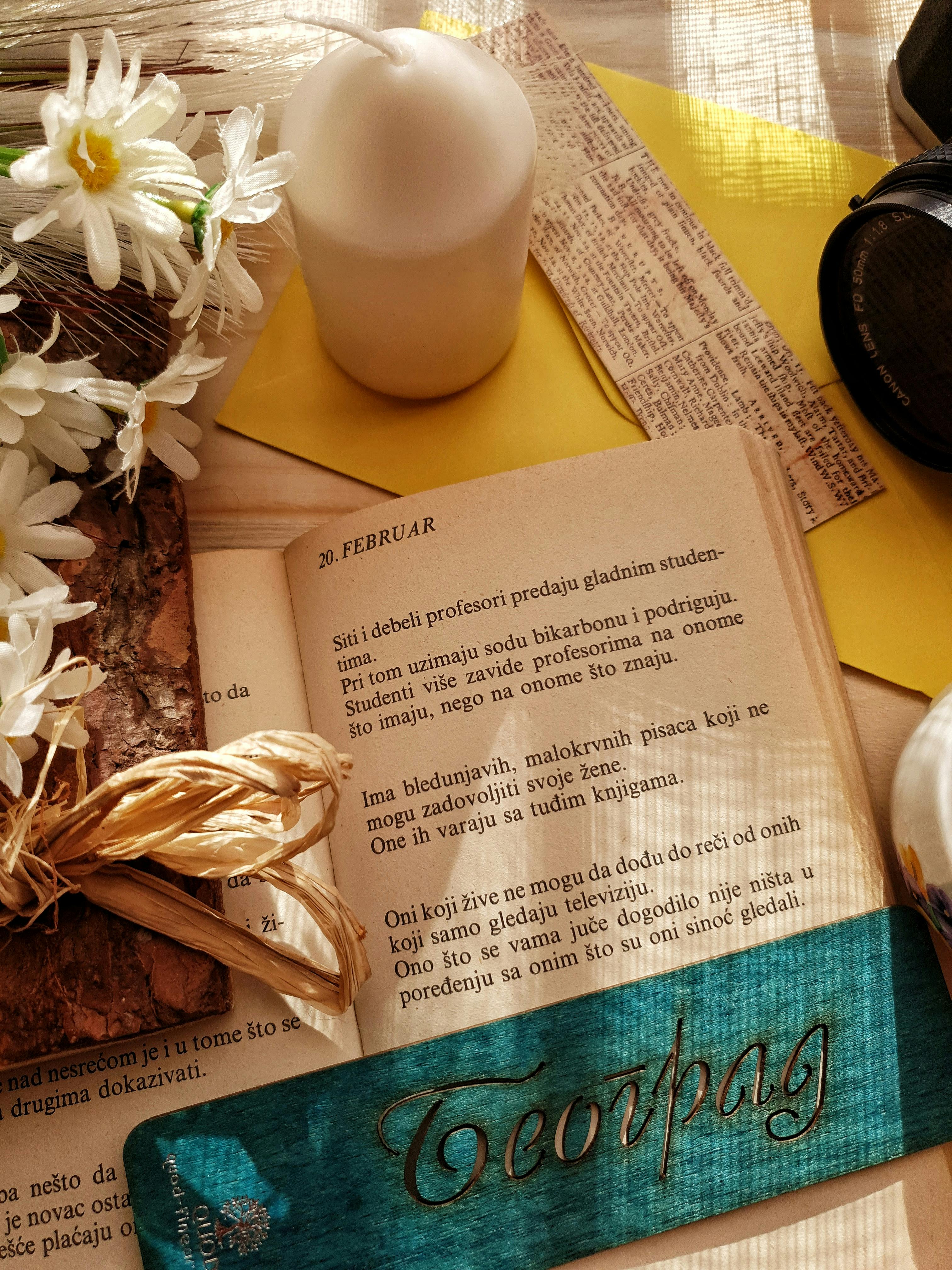 Cozy flat lay of a book with a teal bookmark, candle, and daisies creating a warm, rustic mood.