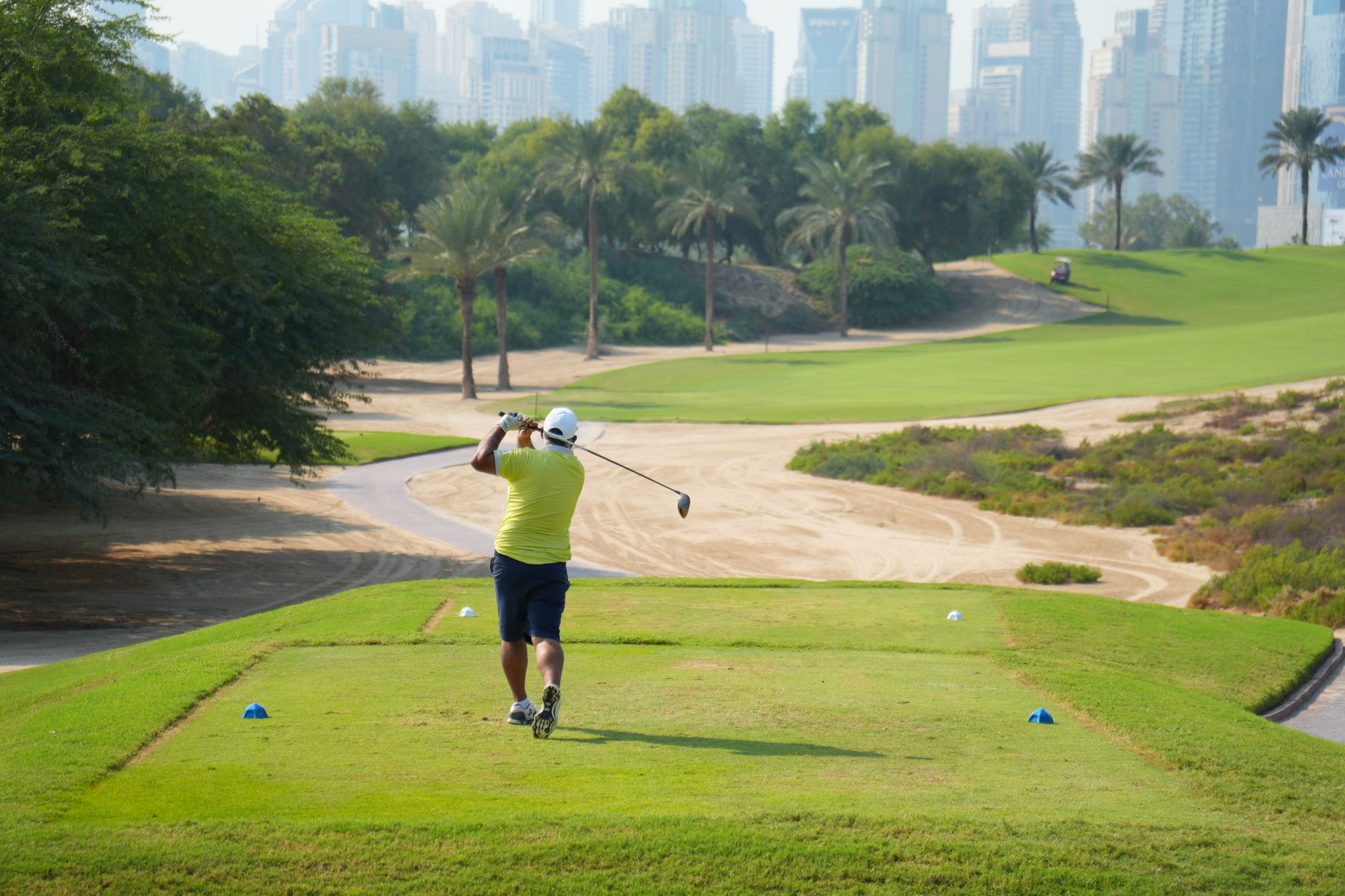 A golfer teeing off on a sunny day with the iconic Dubai skyline in the backdrop.