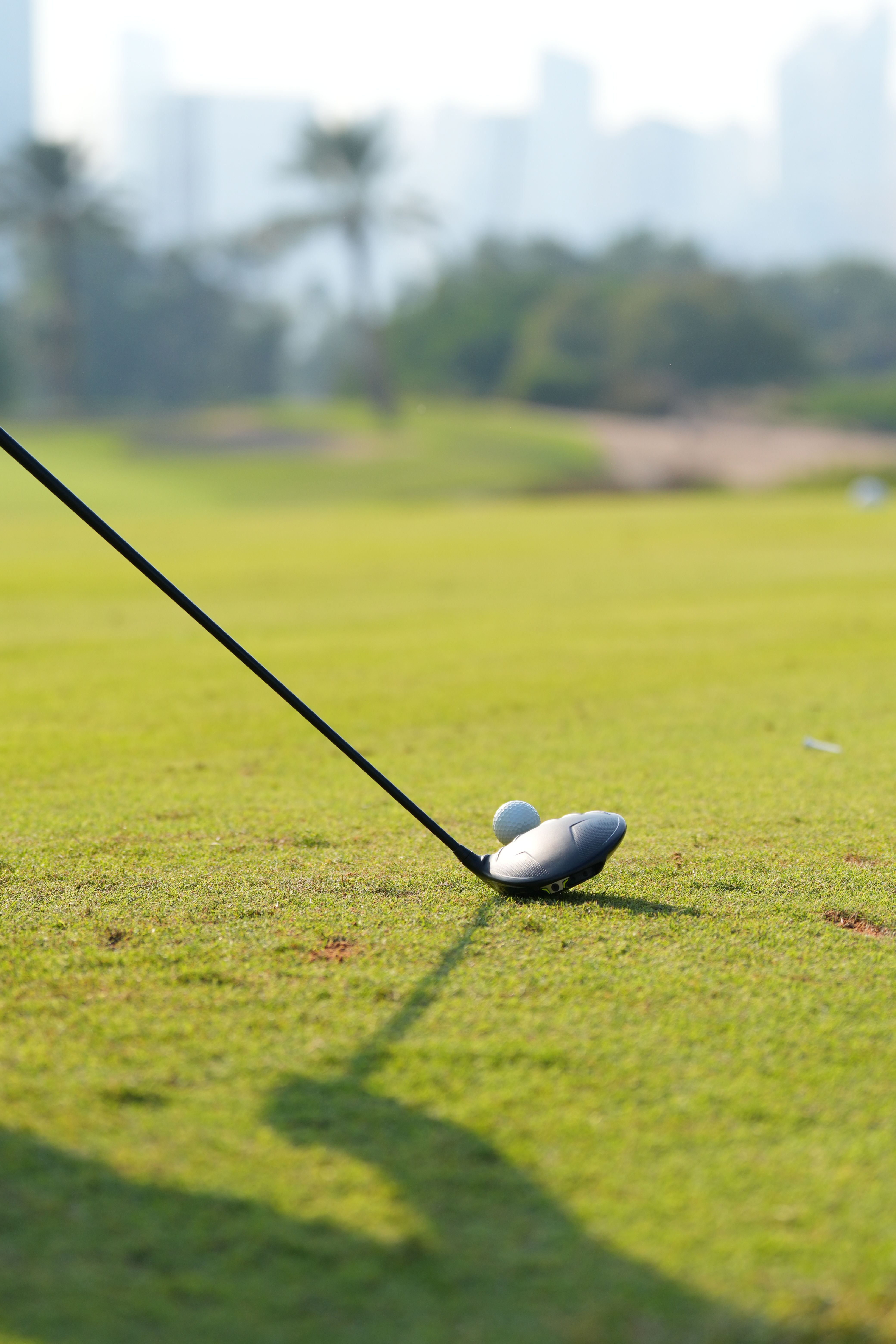 Golf club and ball positioned on a sunny golf course with Dubai skyline blurred in the background.