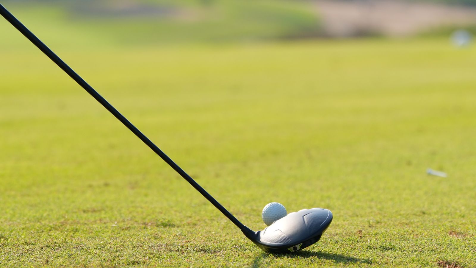 A golf club and ball on a sunny course in Dubai, with the city skyline blurred behind