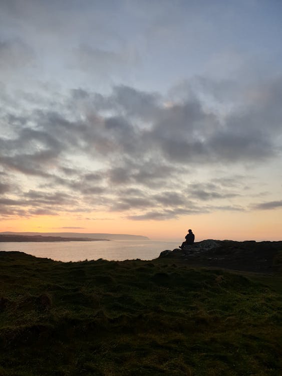 Silhouette of Person Sitting on Rock during Sunset