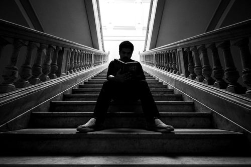 Free Dramatic black and white photo of a student reading on stairs inside a university building. Stock Photo